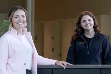 Two students pose for a photo at the welcome desk inside the Quinlan / Brown Academic Innovation Center at Bryant University.